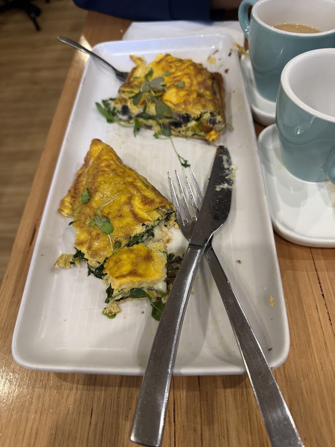 Two slices of spinach and vegetable quiche beside blue mugs of tea at Salt n Pepa Cafe.