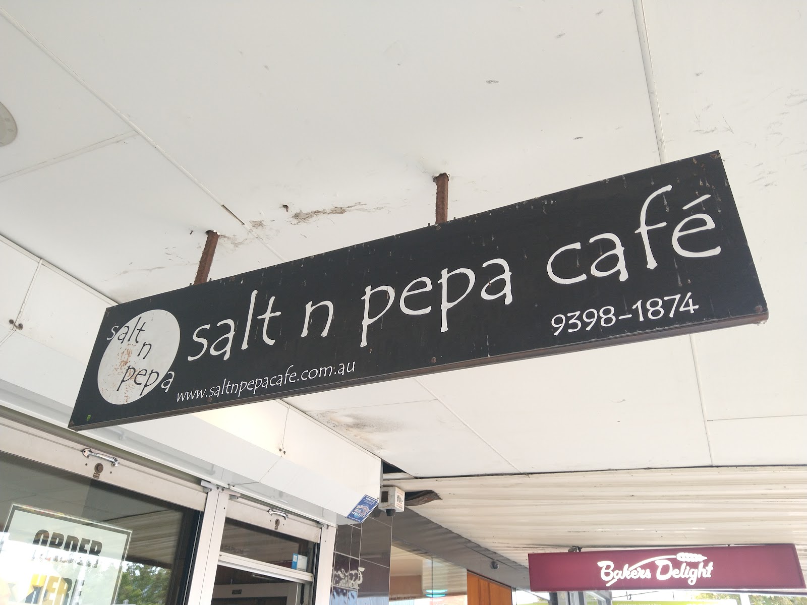 The hand-painted Salt n Pepa Cafe board sign hanging under the awning at 57 Pier Street, Altona.